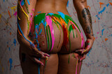 Attractive blonde female posing nude in front of paint splattered background with dripping paint in mulitple colors all over her body