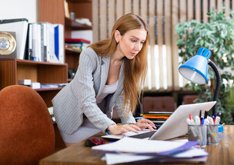 Wall Mural - Portrait of a young business woman in the office near the workplace, typing an important document on a laptop