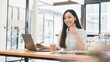 © Satori Studio - Business technology concept, Cheerful young woman giving a thumbs up while working on her laptop at a bright and airy cafe table.