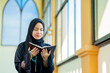 © maya1313 - Ramadan, The image of an Asian Muslim woman in the Islamic religion in hijab in black color. reading the Quran and having a happy smiling face Staying in a beautiful mosque out of respect for God.