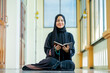 © maya1313 - Ramadan, The image of an Asian Muslim woman in the Islamic religion in hijab in black color. reading the Quran and having a happy smiling face Staying in a beautiful mosque out of respect for God.