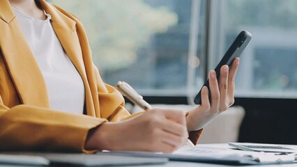 Wall Mural - Woman hand holding white mobile phone on a table with a laptop in office.