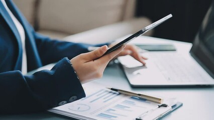 Wall Mural - Woman hand holding white mobile phone on a table with a laptop in office.