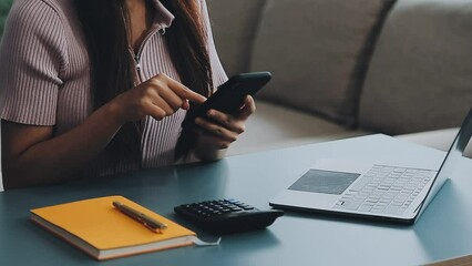 Wall Mural - Woman hand holding white mobile phone on a table with a laptop in office.