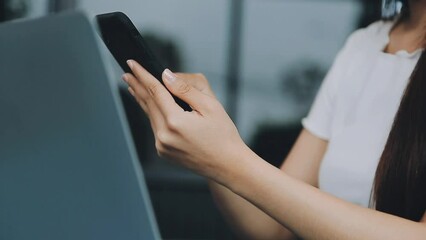 Wall Mural - Woman hand holding white mobile phone on a table with a laptop in office.