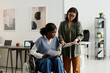 © TrueFrame Collective - Medium long shot of young Caucasian woman showing data on digital tablet to her African American coworker with disability