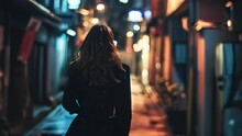 A Young Woman In A Black Coat Is Walking Along The Street At Night.