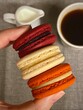 Three macarons in hand with cup of coffee and milk pitcher on the background.