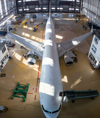 Wall Mural - Top view of a white passenger jetliner in the aviation hangar. Airliner under maintenance. Checking mechanical systems for flight operations