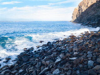 Rocky beach with Atlantic Ocean waves meeting with underwater sharp rocks. Blue sea with small waves with foam crashing on the beach, south of Tenerife, Canary Islands