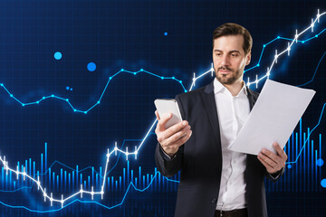 Poster - Attractive young european business man talking on the phone and holding document with glowing and growing business chart on blurry blue background. Financial growth, trade and stock concept.