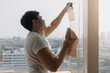 © Sevendeman - Backside view of asian Thai man wiping window glass in room apartment with city view, keep glass sparking clean, house husband and housework concept.