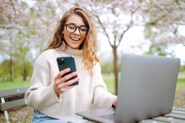 Wall Mural - Happy woman sitting with laptopand phone sitting at a table outdoors . Concept for education, business, shopping, blog or freelance.