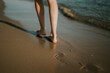 Mujer caminando por la orilla dejando sus huellas en la arena. La huella está enfocada. Puesta de sol en la playa. Date un paseo para desconectar. Ondas suaves y agradables. Hermosas piernas de mujer.