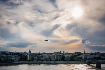  An old biplane flying over the evening city of Novi Sad, Serbia against the background of amazing clouds. Chemical treatment of the territory from mosquitoes and insects