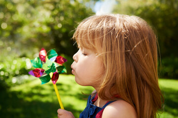 Poster - Young girl, outdoor and blowing pinwheel, garden and enjoying freedom of outside and happy. Pretty little child, backyard and summer for playing, toy and windmill for school holidays and happiness