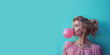 une jeune femme blonde gonfle une bulle de chewing gum devant un fond bleu - vue de profil