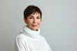 © photolas - An elderly beautiful woman with dark colored short cut hair. Old model in white knitted sweater poses on light gray background.