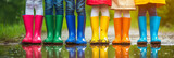 Fototapeta Na drzwi - Close-up on children legs in colorful wellie boots standing in a puddle. Kids jumping over puddles in colorful rain boots.