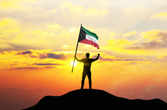 Kuwait flag being waved by a man celebrating success at the top of a mountain against sunset or sunrise. Kuwait flag for Independence Day.