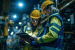 © Old Man Stocker - Two engineers in safety gear discuss over a digital tablet against the backdrop of heavy machinery in a manufacturing plant.