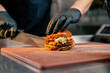 close-up of the hands of a chef in an establishment cutting a ready-made burger lying on board with a knife