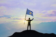 Kosovo flag being waved by a man celebrating success at the top of a mountain against sunset or sunrise. Kosovo flag for Independence Day.