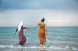 © Connect Images - Two young women, best friends one is wearing a hijab having fun and enjoying time at the beach.
