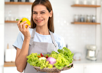 Young adult smiling lovely housewife standing in kitchen preparing fresh healthy vegan salad essential green vegetables and trying new recipe. Enjoyment dieting healthy nutrition lifestyle.