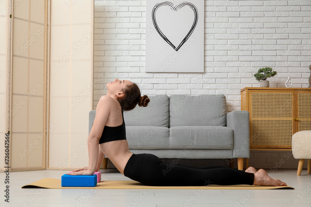 Sporty young woman practicing yoga with blocks at home