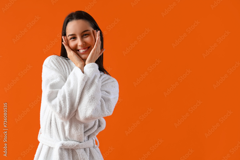Young woman in bathrobe on orange background