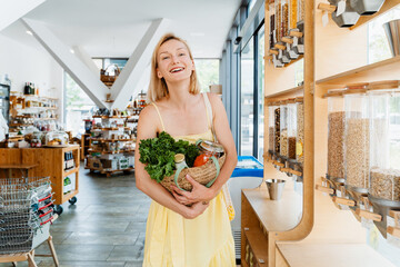 Wall Mural - Smiling woman with basket of organic products in sustainable plastic free store. Dispensers for cereals, grains, nuts at zero waste shop.