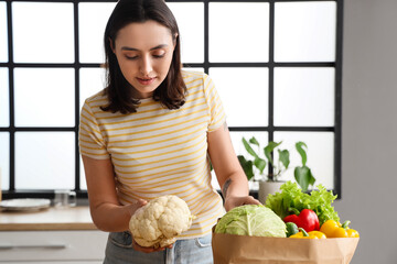 Wall Mural - Young woman with paper bag of fresh vegetables in kitchen