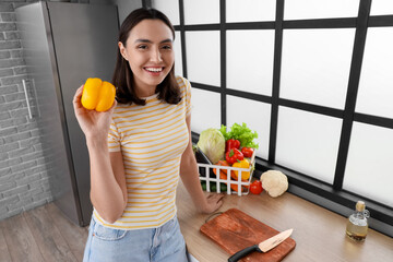 Wall Mural - Young woman with bell pepper in kitchen