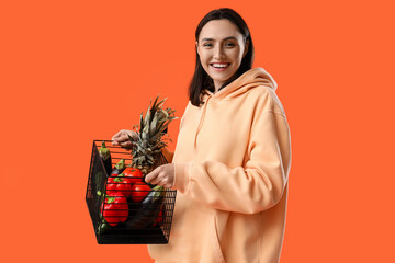 Wall Mural - Young woman with basket of healthy food on orange background