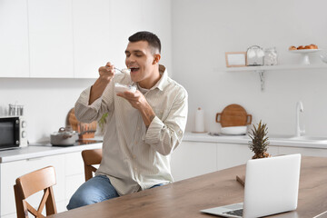 Wall Mural - Young man eating tasty yogurt in kitchen