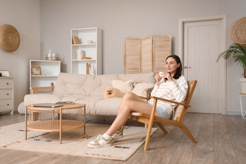 Sticker - Happy young woman with cup of coffee in wooden armchair and Pomeranian dog at home