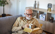© Jelena Stanojkovic - Close up of old happy and relaxed man sitting reading a book at home. Mature male person enjoying free time having fun indoor.