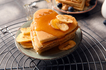 Plate with tasty pancakes in shape of heart and dried banana on grey tile background, closeup. Valentine's Day celebration