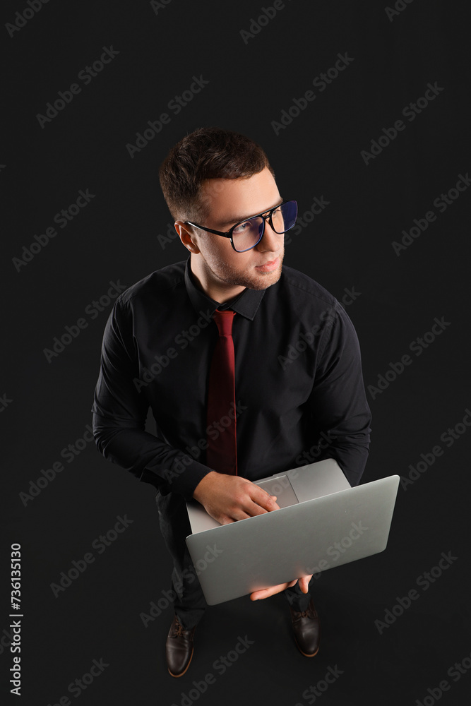 Handsome businessman in eyeglasses working with laptop on black background