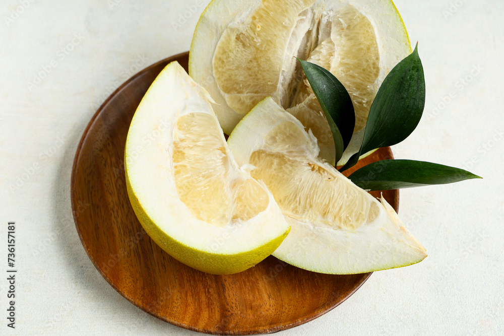 Wooden plate with cut fresh pomelo fruit and leaves on white background