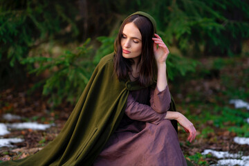 Portrait of Amazing fairytale princess in elven green cape and vintage dress standing in winter forest with red berries. Warm art work with queen elegant vintage lady.