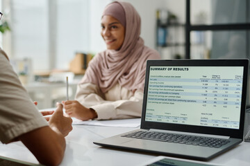 Leinwandbilder - Financial data on screen of laptop standing on desk next to young Muslim businessman explaining something to female colleague in hijab