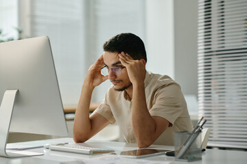 Leinwandbilder - Young stressed male employee sitting by desk in front of computer screen and waiting for page uploading while trying to concentrate