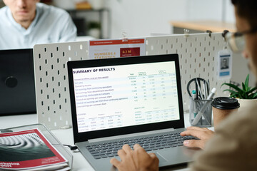 Leinwandbilder - Laptop screen with summary of results and hands of young male economist typing on keyboard while sitting by workplace
