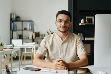 Poster - Young Muslim male ceo or entrepreneur sitting by workplace with desktop computer in coworking space and looking at camera