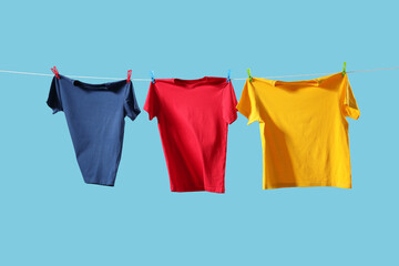 Sticker - Colorful t-shirts drying on washing line against light blue background