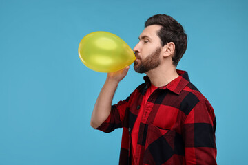 Wall Mural - Man inflating yellow balloon on light blue background. Space for text