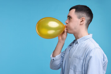 Canvas Print - Young man inflating golden balloon on light blue background