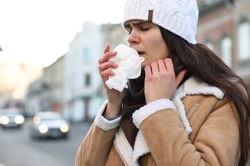 Poster - Woman with tissue blowing runny nose outdoors. Cold symptom